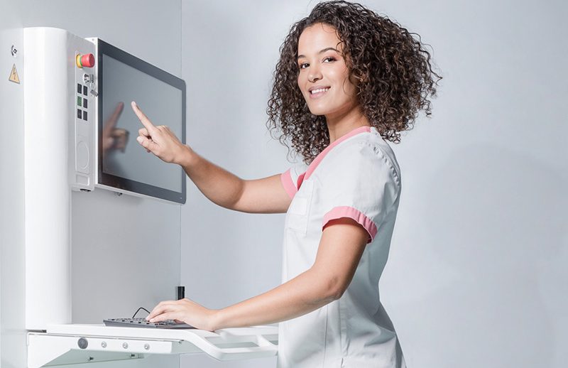 A nurse pointing at a screen and smiling at the camera
